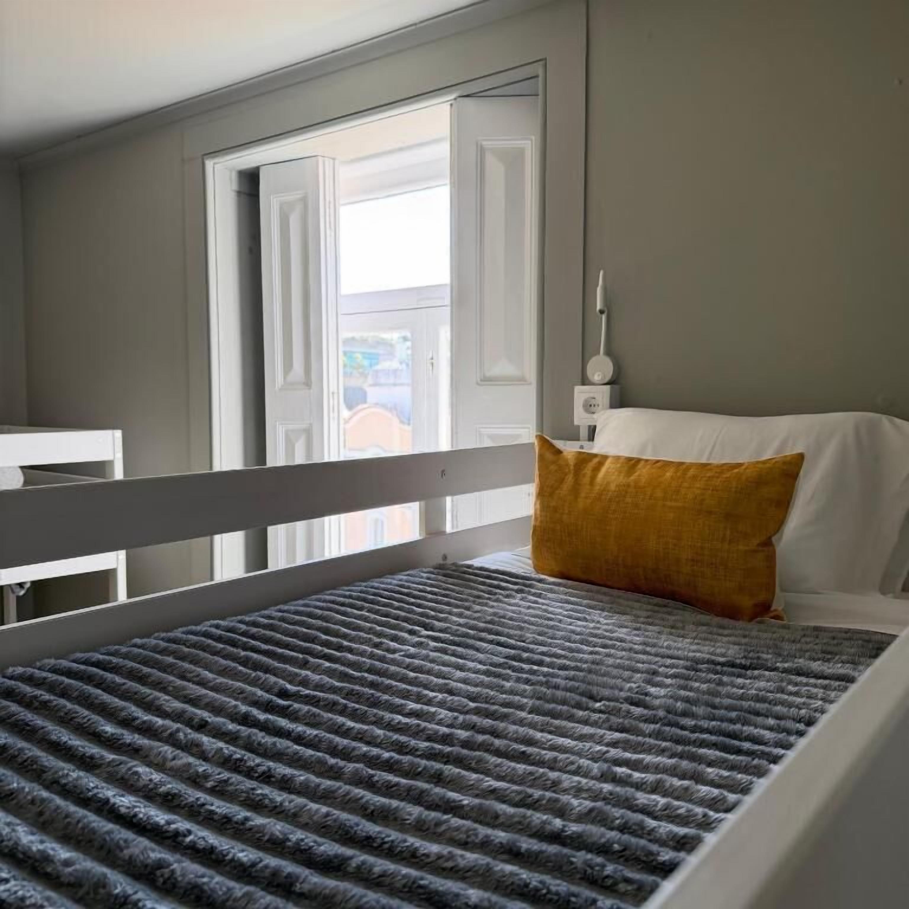 A bed with a grey textured mattress, a white headboard, and a mustard-colored pillow.