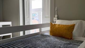 A bed with a grey textured mattress, a white headboard, and a mustard-colored pillow.