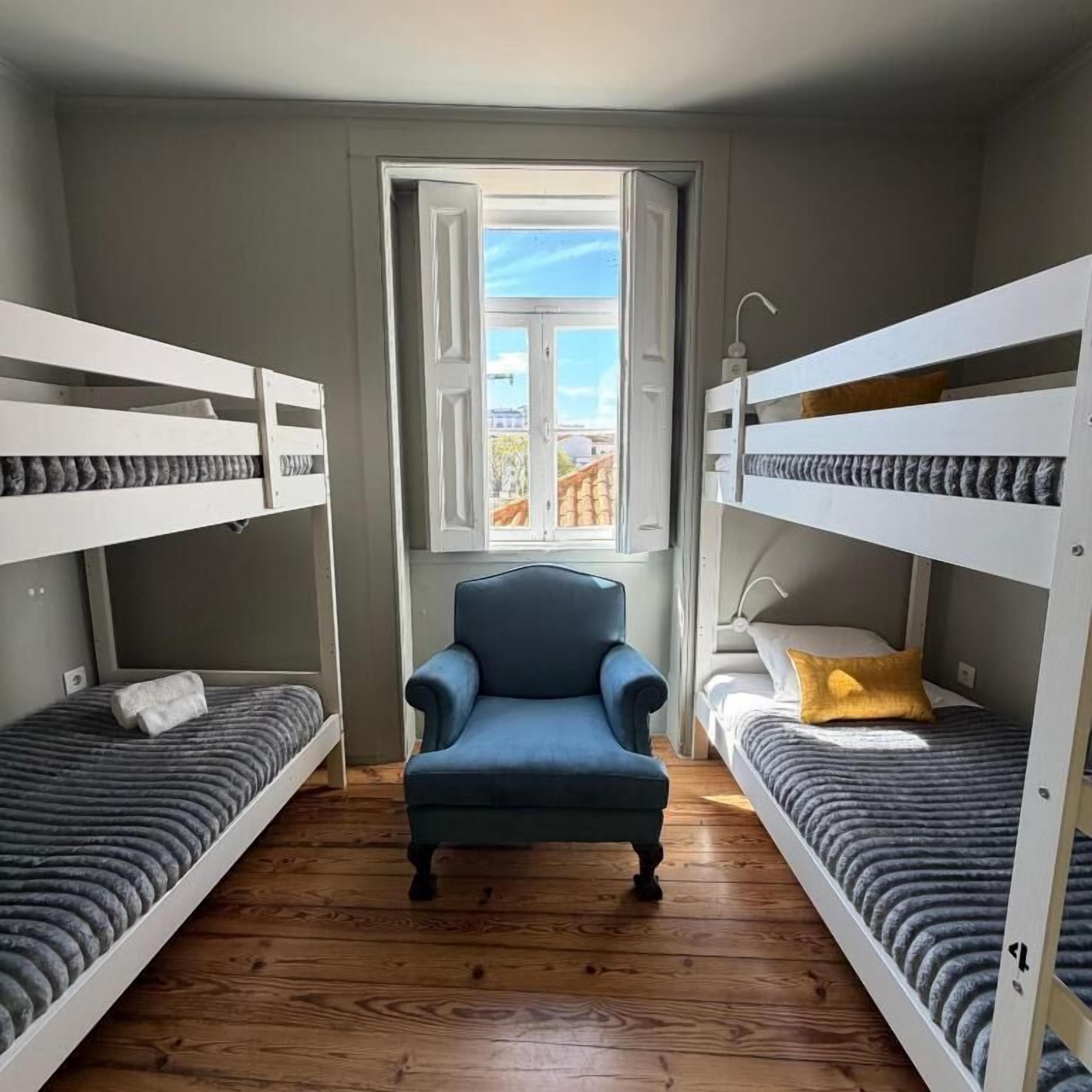 A room with bunk beds, a chair, and a window with an open door.