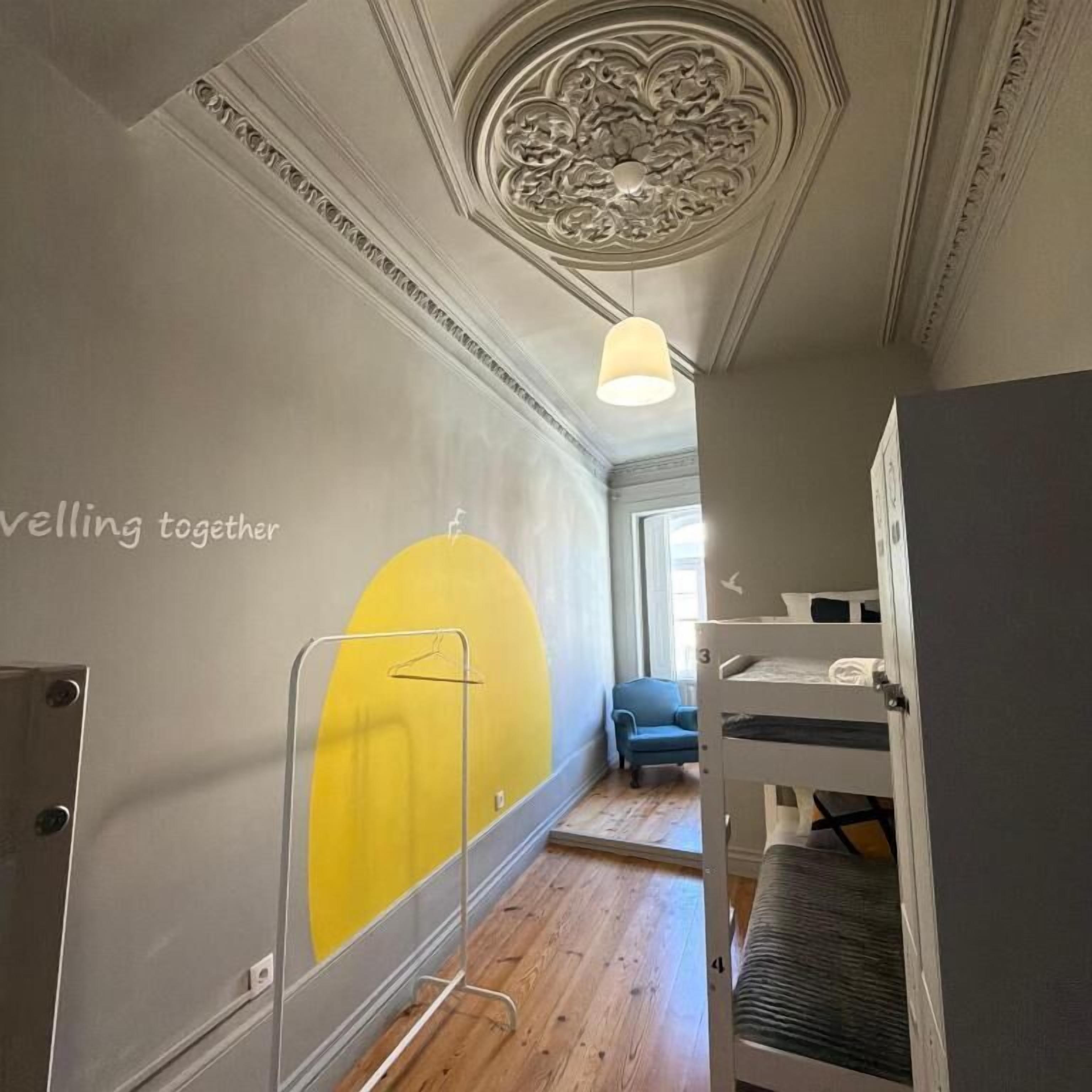 A room with bunk beds, a yellow wall mural, a ceiling with intricate molding, and a hanging light fixture.