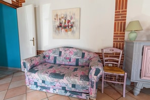 Ein Zimmer mit einer gemusterten Couch, einem Sessel, einer Lampe und einem Bild an der Wand.