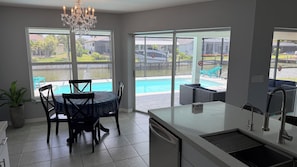 Eine Küche mit Essbereich, großen Fenstern, einem Chandelier und Blick auf einen Swimmingpool.