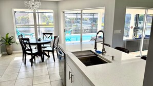 A kitchen with a white countertop, a sink, and a dining area with chairs and a table. - Relaxing House with Gulf Access & Heated Pool (Cape Coral)