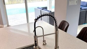 A modern kitchen with a stainless steel sink, a wooden cutting board, and a view of a pool outside. - Relaxing House with Gulf Access & Heated Pool (Cape Coral)