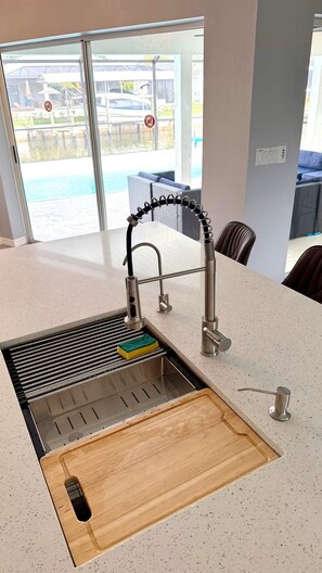 Eine moderne Küche mit Spüle aus Edelstahl, Schneidebrett aus Holz und Blick auf einen Pool.