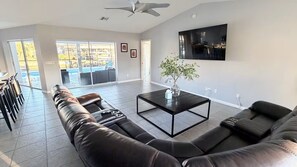 Ein großzügiger Wohnraum mit Ecksofa, Couchtisch und an der Wand befestigtem Fernseher.