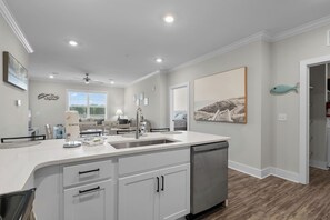 A modern kitchen with a large island, white cabinetry, and a dishwasher. - 1610 Crow Creek Drive (Calabash)