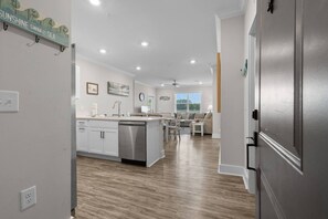 A modern kitchen with a central island, a dining area with a table and chairs, and a living room with a sofa. - 1610 Crow Creek Drive (Calabash)