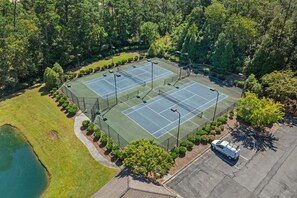 Ein Luftbild eines Tennisplatzkomplexes, umgeben von Bäumen, mit einem Parkplatz und einem kleinen Gewässer.