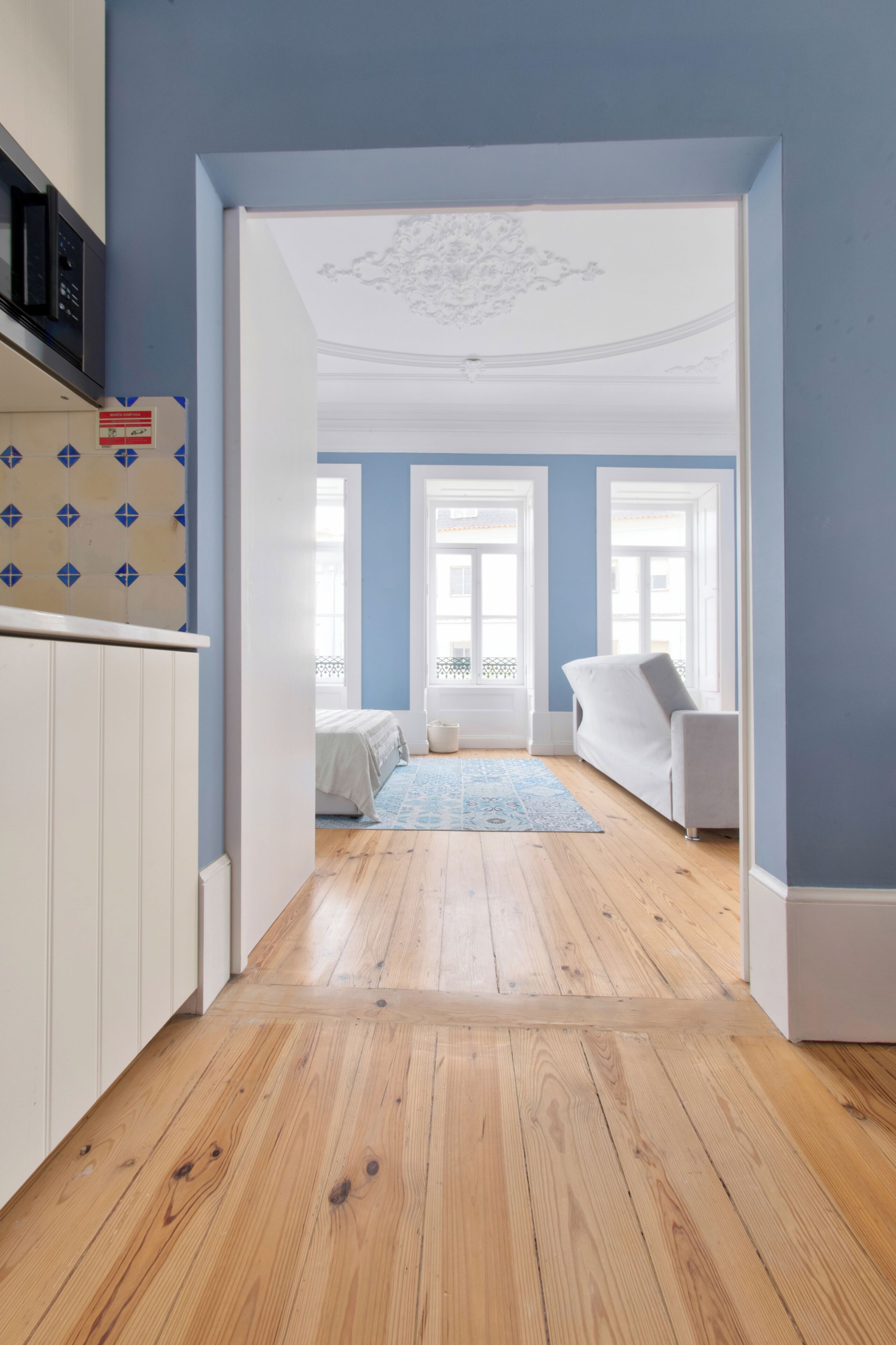 A room with a wooden floor, a white sofa, and a bed with a blue rug.