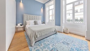 A bedroom with a large bed, a bedside table, a nightstand, a window with a view, and a patterned rug. - Aveiro History Apartments (Aveiro)