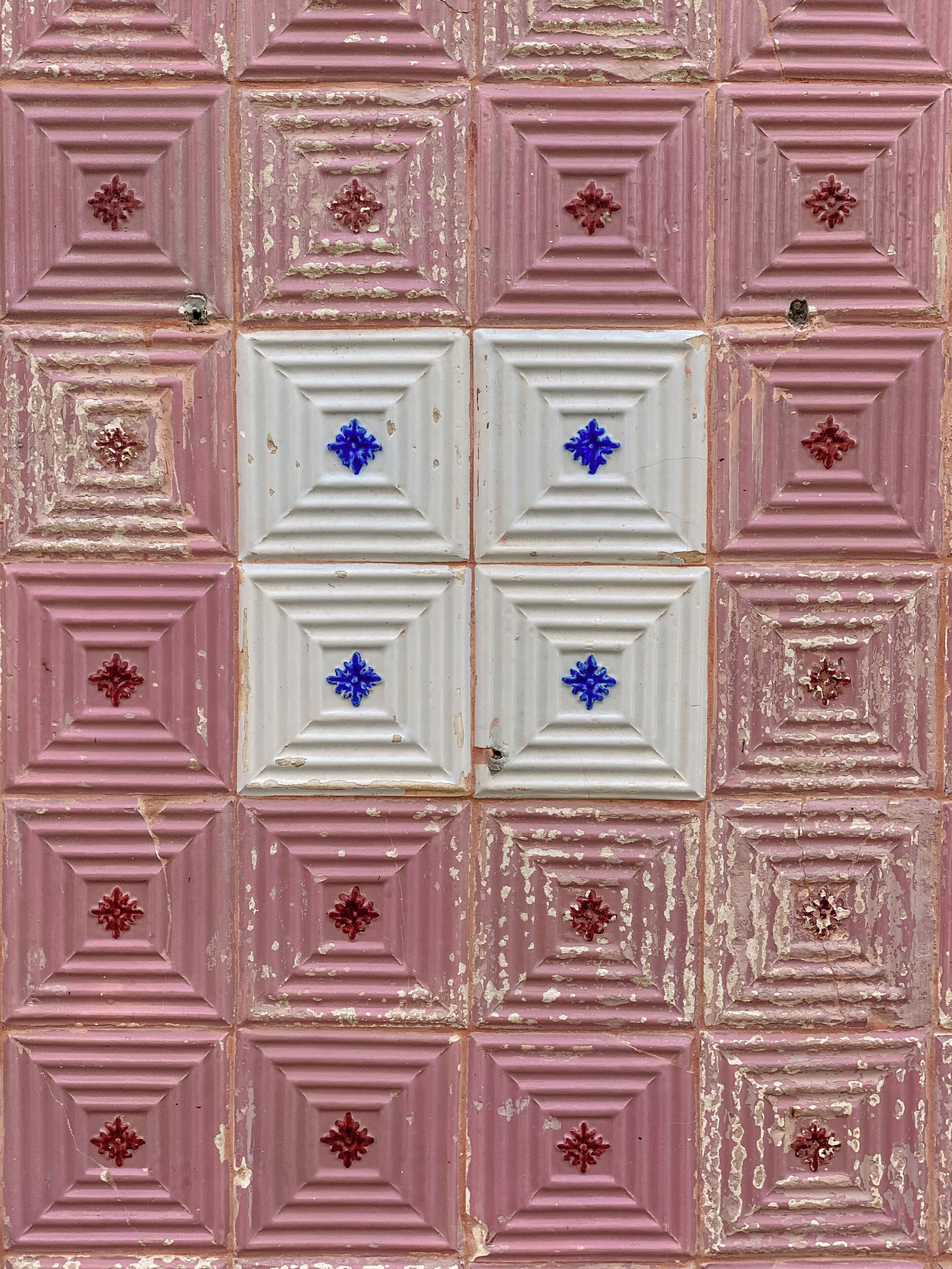 Un mur orné d’un motif composé de carreaux carrés alternant les couleurs rose et blanc, dont certains présentent des motifs floraux.