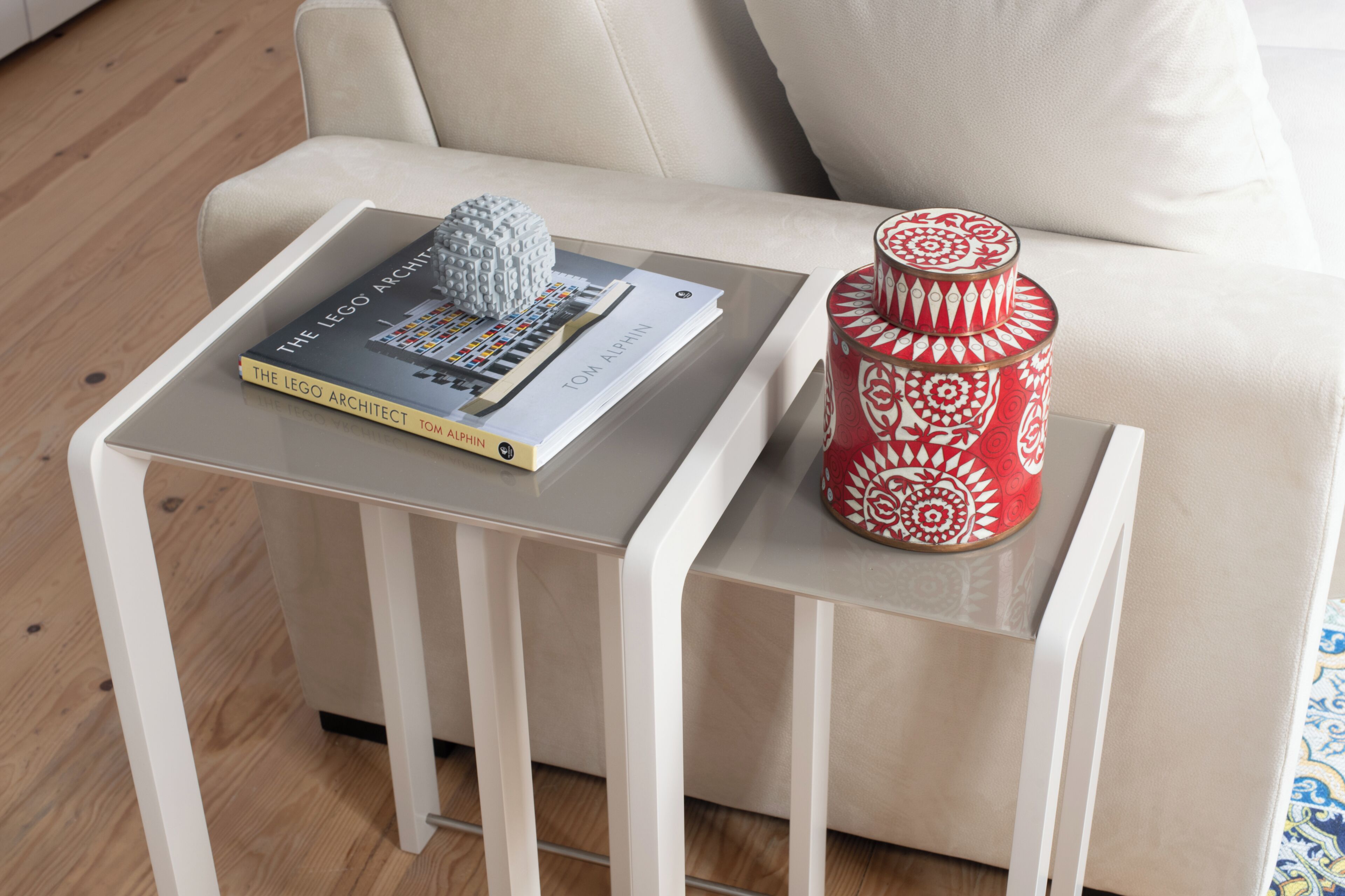 A modern living room with a sofa, a side table with a book titled 'The LEGO Architect' and a decorative item.