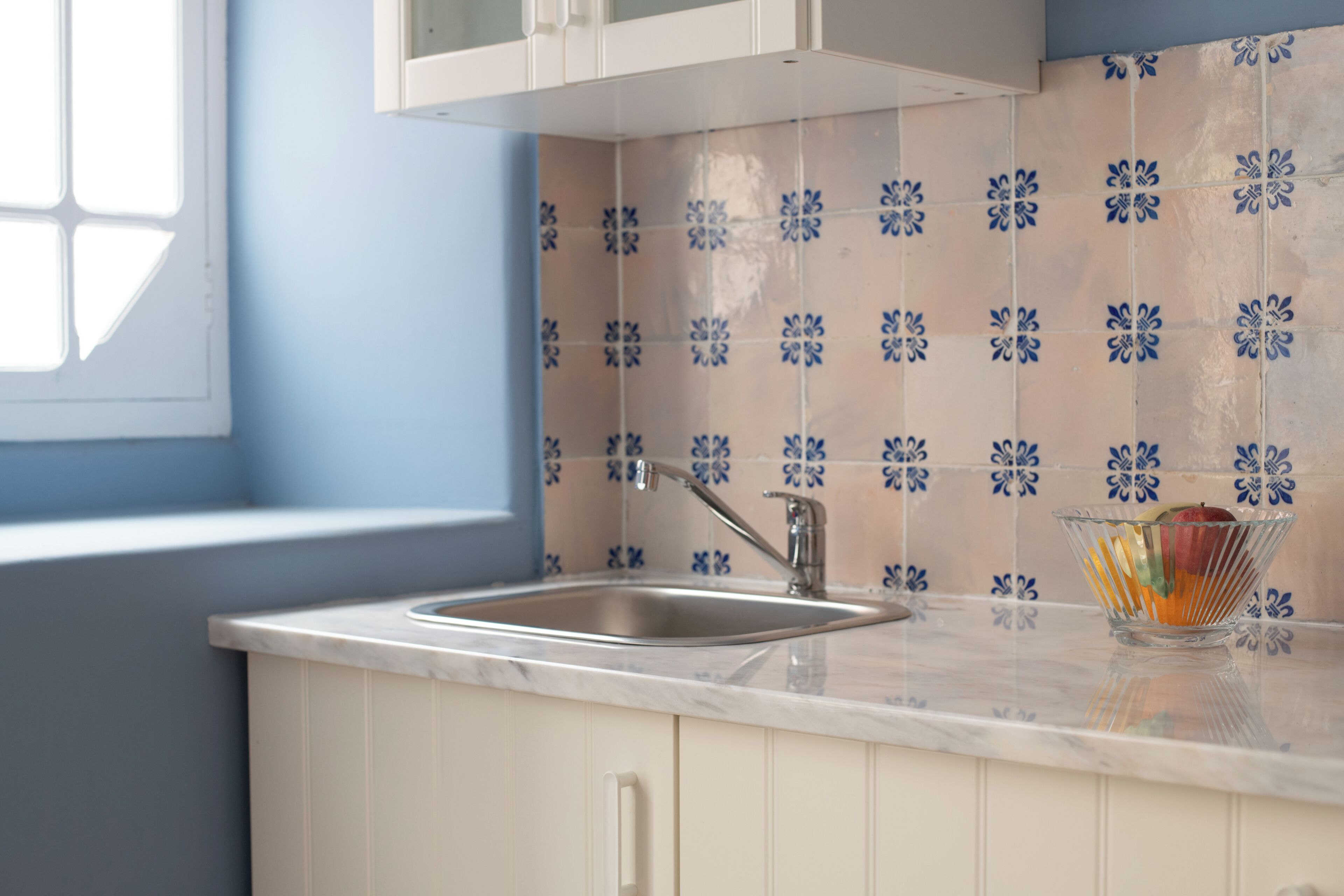 A kitchen with a sink, a window, and a bowl of fruit on the counter.