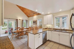 A kitchen with white cabinets, a granite countertop, a wooden dining table with chairs, and a view through the glass door. - Private Coastal 4 BD Getaway in Ocean Park ME (Old Orchard Beach)