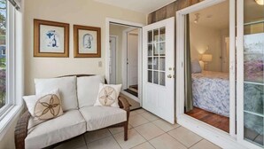 A room with a white sofa, two framed pictures on the wall, a wooden door, and a view through a glass door. - Private Coastal 2 BD Residence in Ocean Park ME (Old Orchard Beach)