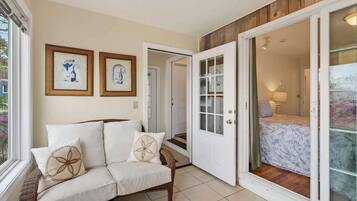A room with a white sofa, two framed pictures on the wall, a wooden door, and a view through a glass door.