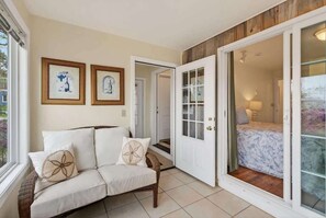 Ein Zimmer mit einem weißen Sofa, zwei gerahmten Bildern an der Wand, einer Holztür und Blick durch eine Glastür.