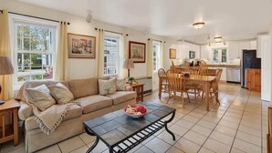 A spacious living room with a sofa, dining table, and chairs, a kitchen area with cabinets and appliances, and large windows with curtains. - Private Coastal 2 BD Residence in Ocean Park ME (Old Orchard Beach)