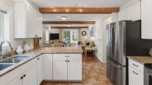 A kitchen with white cabinets, granite countertops, a stainless steel refrigerator, and a dining area with a table and chairs. - Private Coastal 3 BD Residence in Ocean Park (Old Orchard Beach)