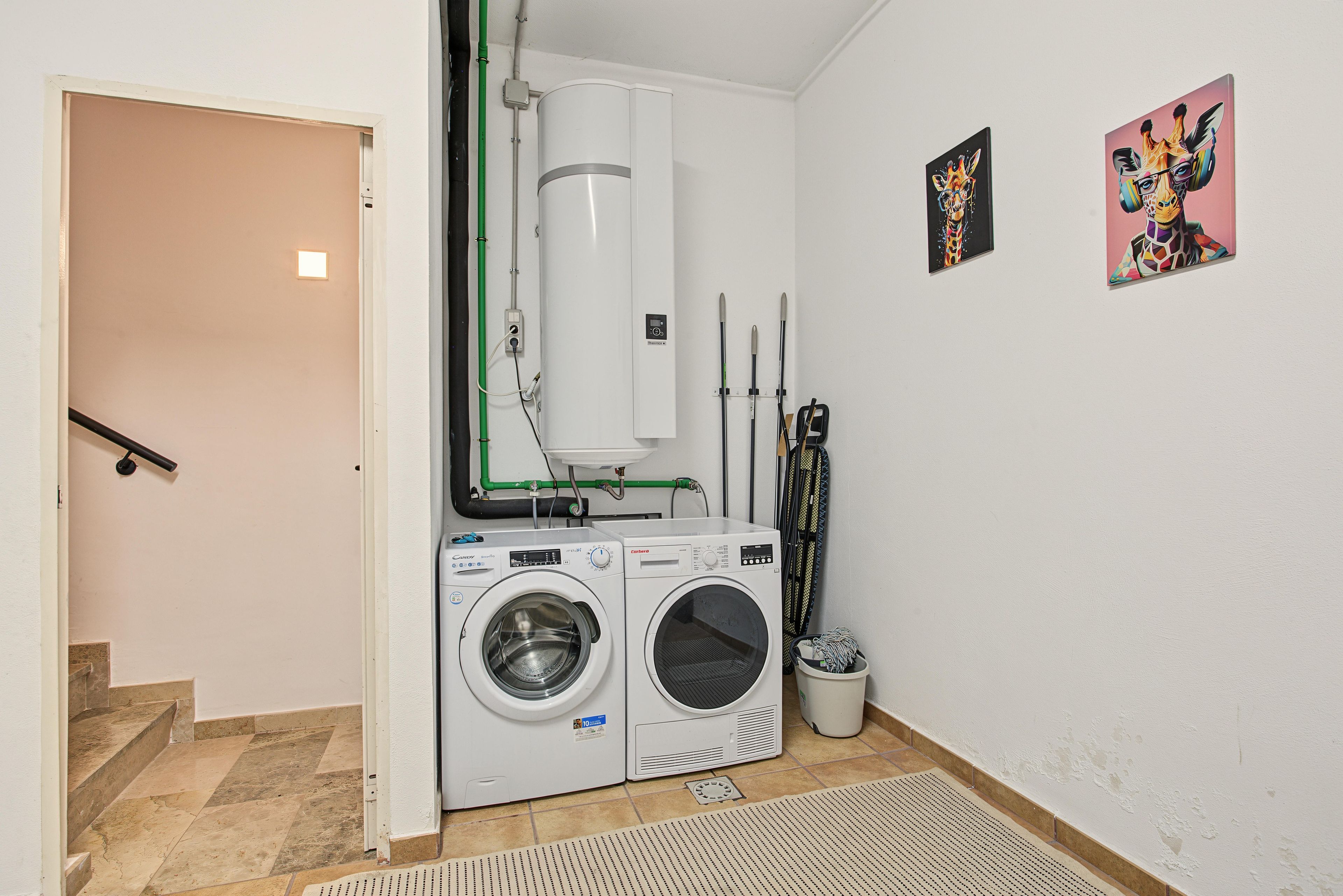 A laundry room with two washing machines, a water heater, and a radiator.