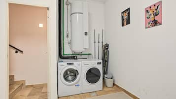 A laundry room with two washing machines, a water heater, and a radiator.