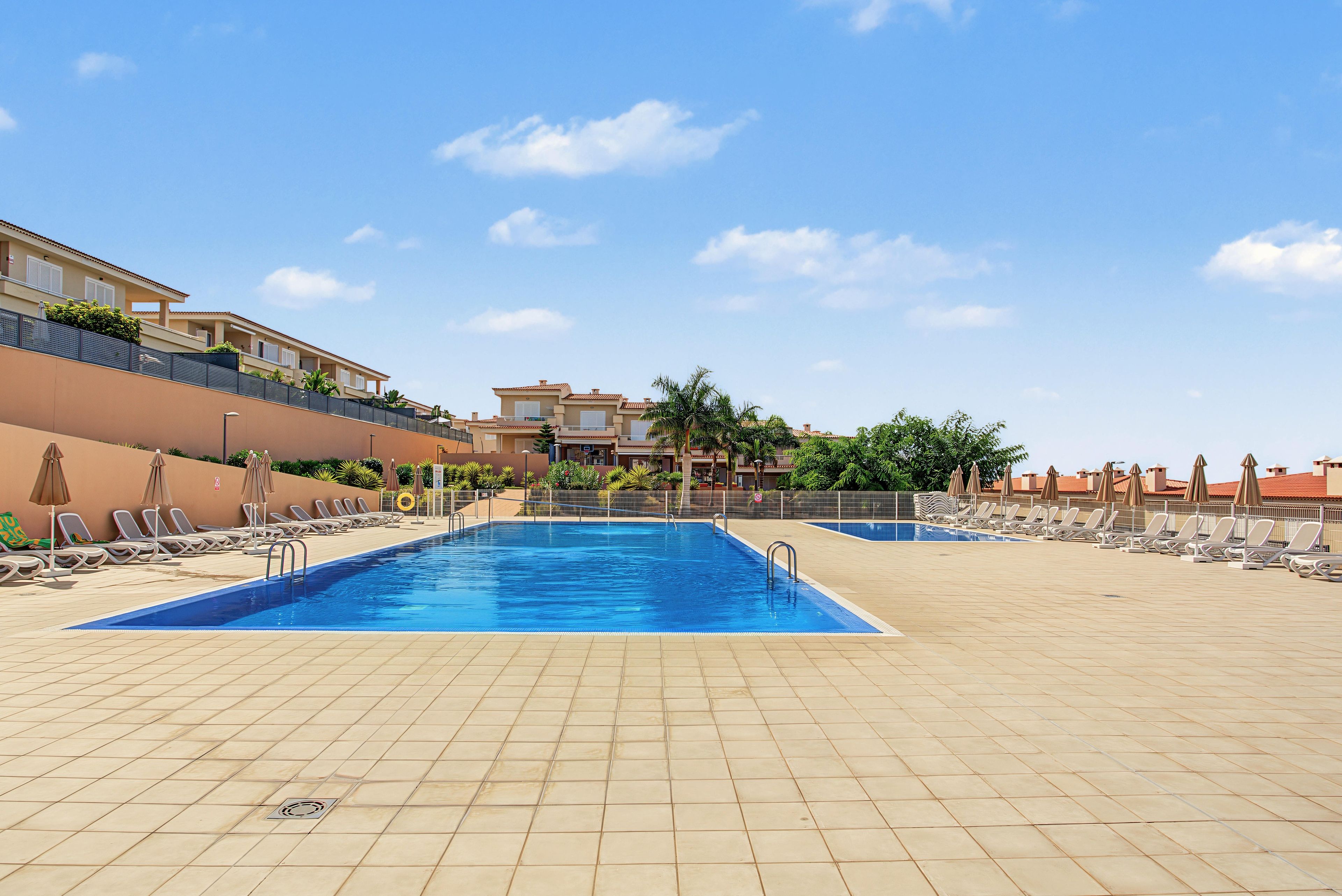 Ein Schwimmbecken mit Liegestühlen und Sonnenschirmen, umgeben von einer gefliesten Terrasse.