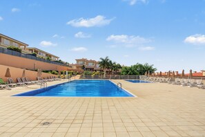 A swimming pool with sun loungers and umbrellas, surrounded by a tiled deck.