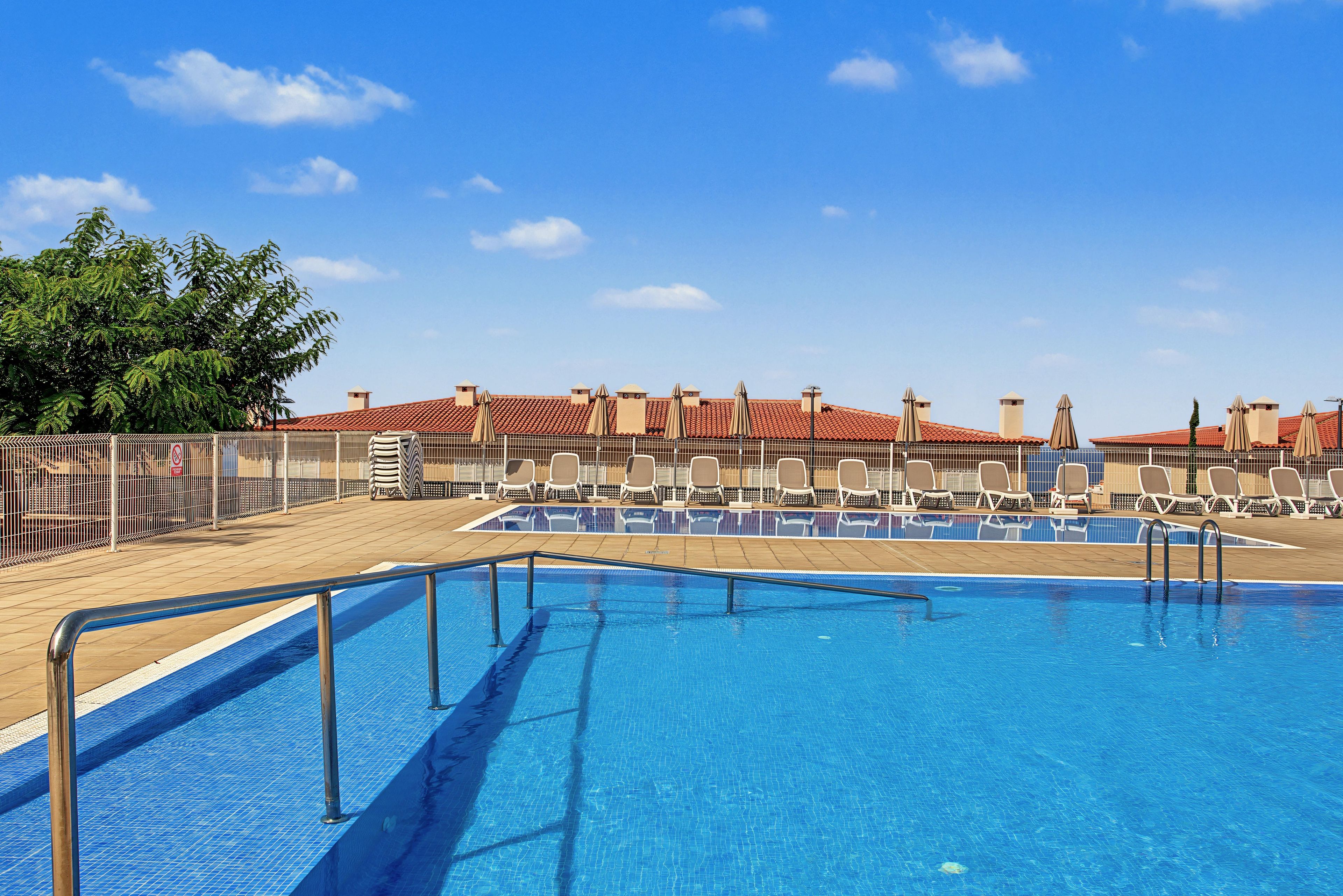 A swimming pool with a tiled deck, lounge chairs, and a fenced area with a no swimming sign.