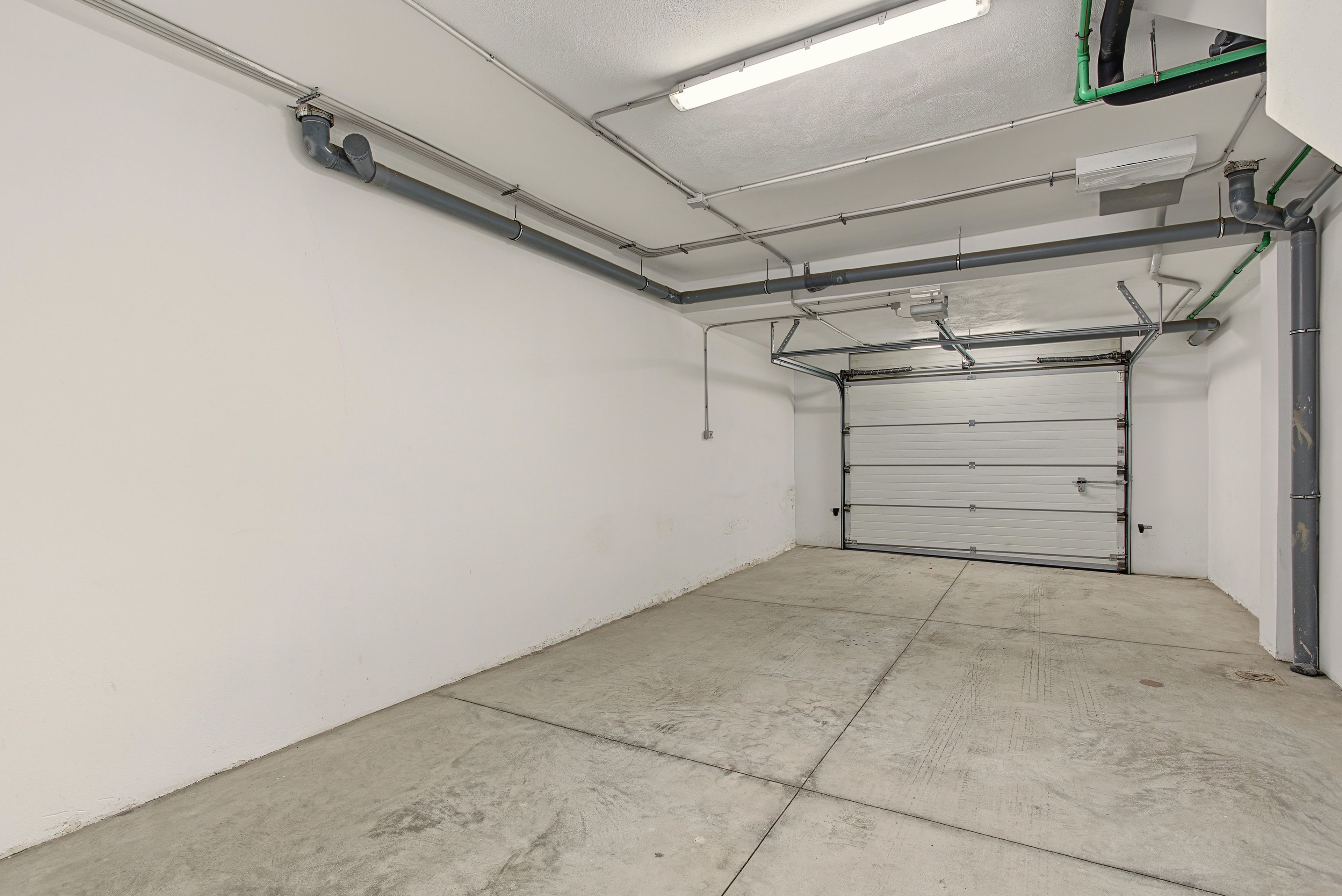 Eine saubere, leere Garage mit geschlossenem Garagentor, Betonboden und Deckenleuchten.
