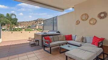 An outdoor patio with a sofa, a table, and a hot tub.