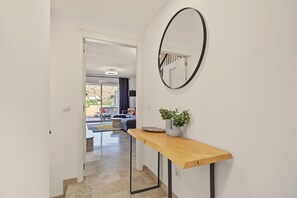 A hallway with a wooden console table, a potted plant, and a round mirror on the wall.