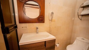 Un baño con lavamanos blanco, tocador de madera, un espejo, inodoro y un perchero para toallas.