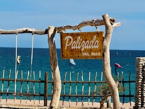 A wooden sign with 'Polizada Del Mar' written on it, a wooden fence, and the ocean in the background.