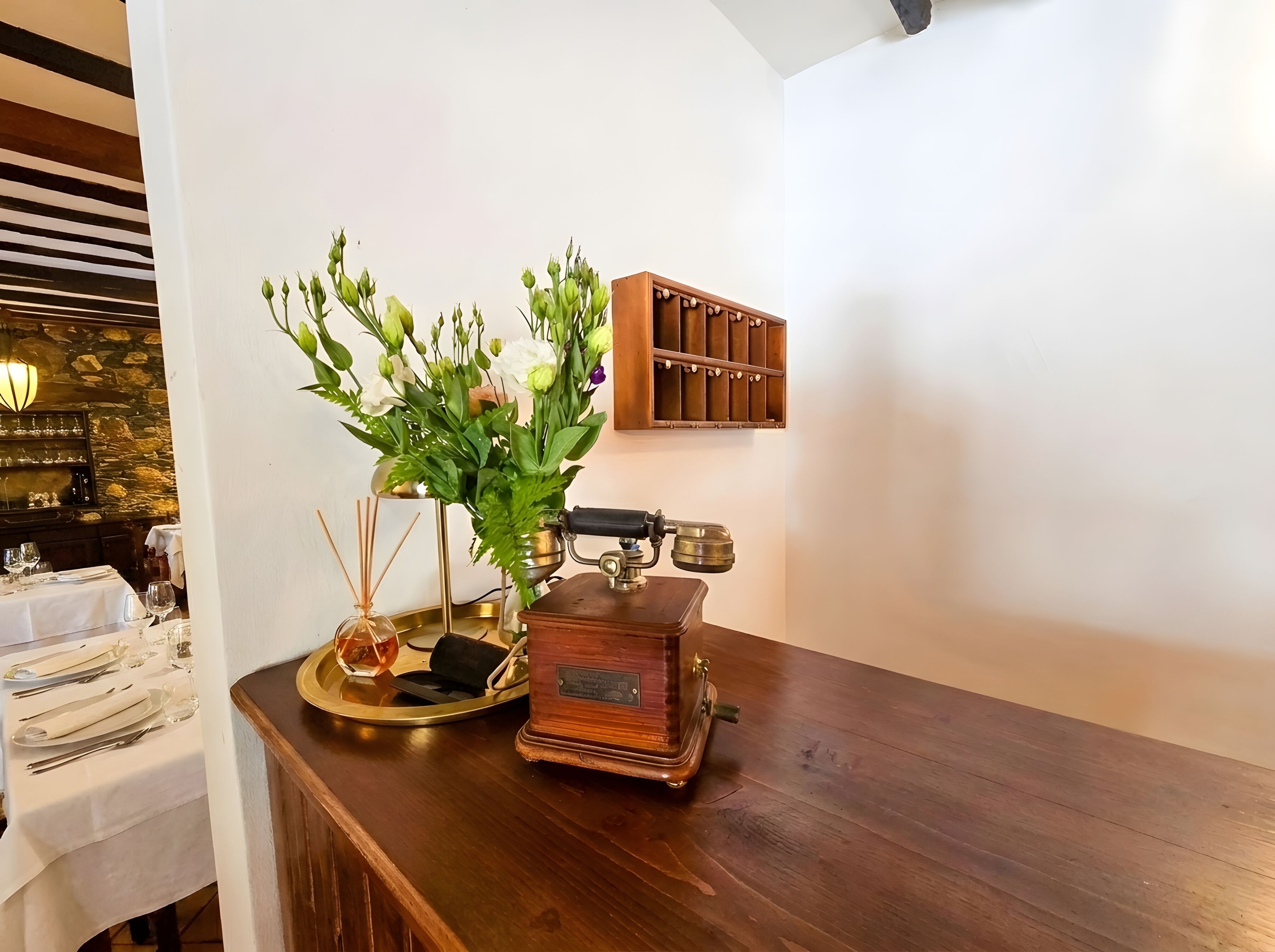 A wooden table with a vintage radio, a glass vase with flowers, and a tray with a candle.