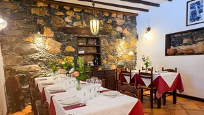 Un restaurante con paredes de piedra, vigas de madera y mesas dispuestas con manteles blancos y servilletas rojas.