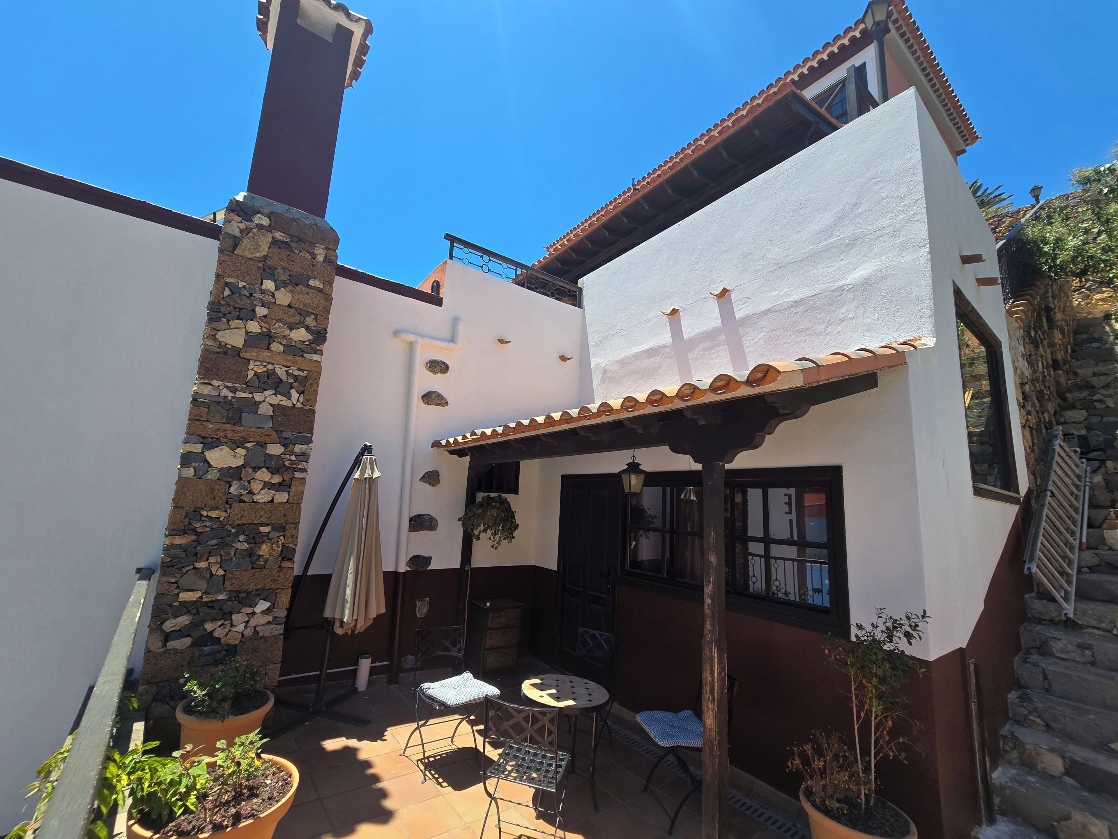 Une terrasse avec des meubles d’extérieur, un mur en pierre et un bâtiment blanc doté d’un toit en tuiles.