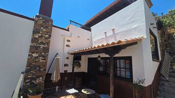 Une terrasse avec des meubles d’extérieur, un mur en pierre et un bâtiment blanc doté d’un toit en tuiles.