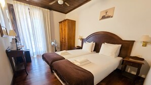 Habitación de hotel con una cama grande, cabecera de madera, dos mesitas de noche con lámparas, un armario de madera y un ventilador de techo.