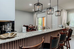 Uma cozinha moderna com bancada de granito, cadeiras de madeira e iluminação pendente.