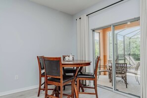A dining area with a round table and chairs, a window with curtains, and a view of the outdoors. - 5BR Private Pool Home at Veranda Palms (Kissimmee)