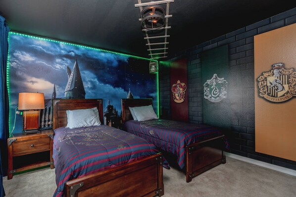 A room with two beds, a nightstand, a lamp, a wall with a crest, and a starry sky mural. - 5BR Private Pool Home at Veranda Palms (Kissimmee)