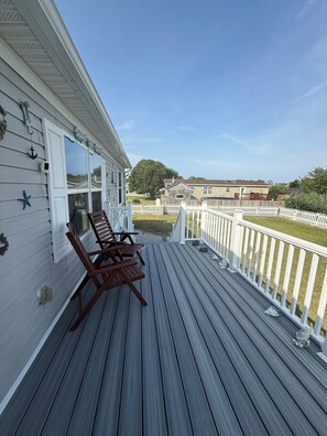 A wooden deck with two rocking chairs, a white fence, and a view of neighboring houses. - Stay Under the Stars in Chincoteague (Chincoteague)