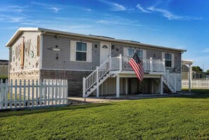 A two-story house with a white picket fence, a front porch, and an American flag.