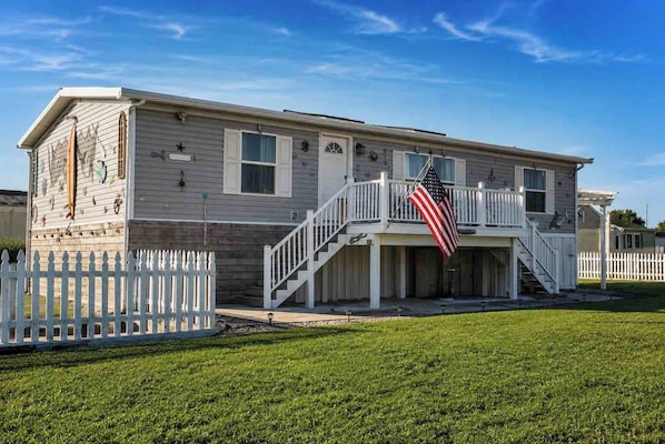 A two-story house with a white picket fence, a front porch, and an American flag.