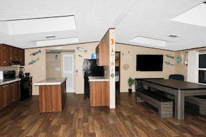 A modern kitchen with wooden cabinets, a central island, and a dining area with a long table.