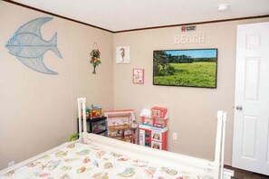 Habitación infantil con cama, juguetes, decoración de pez en la pared, un cuadro con motivos playeros y un cartel que dice 'NO FUMAR'.