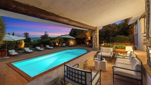 A swimming pool with lounge chairs and a table, surrounded by stone walls and plants. - Villa Althaea 6, Emma Villas (Orbetello)