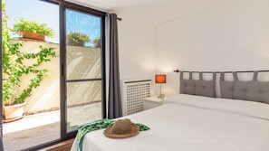 Ein Schlafzimmer mit Bett, Nachttisch, Lampe, einem Fenster mit Vorhängen und Blick ins Freie.