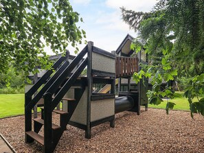 A playground with a slide and climbing area, surrounded by trees and a grassy area.